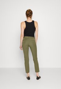 Mörk tanktopp, olivgrön passformade byxor med bakfickor, kort längd, slät textur, i kombination med svarta slip-on skor.