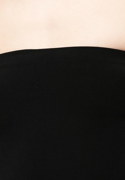 Άνω μέρος στήθους και ώμοι με λεία, ανοιχτόχρωμη επιδερμίδα, που φορούν μαύρο ρούχο χωρίς τιράντες σε ουδέτερο φόντο.