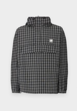 Μαύρο και λευκό πουλόβερ με καρό σχέδιο, ψηλό γιακά, εμπρόσθιο καπάκι τσέπης και ελαστικά μανσέτα, παρουσιασμένο σε λευκό φόντο.