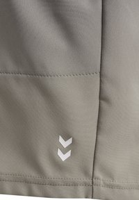 Nærbillede af lyst gråt stof med to hvide chevron-symboler pegende nedad og synlige sømme langs samlingerne.