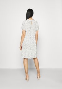 Kukkamekko valkoisena, jossa on sinisiä ja vihreitä kuvioita, lyhyet hihat, avainaukkotakaosa ja koota vyötäröllä, virtaava kerroksittain viimeistelty helma.