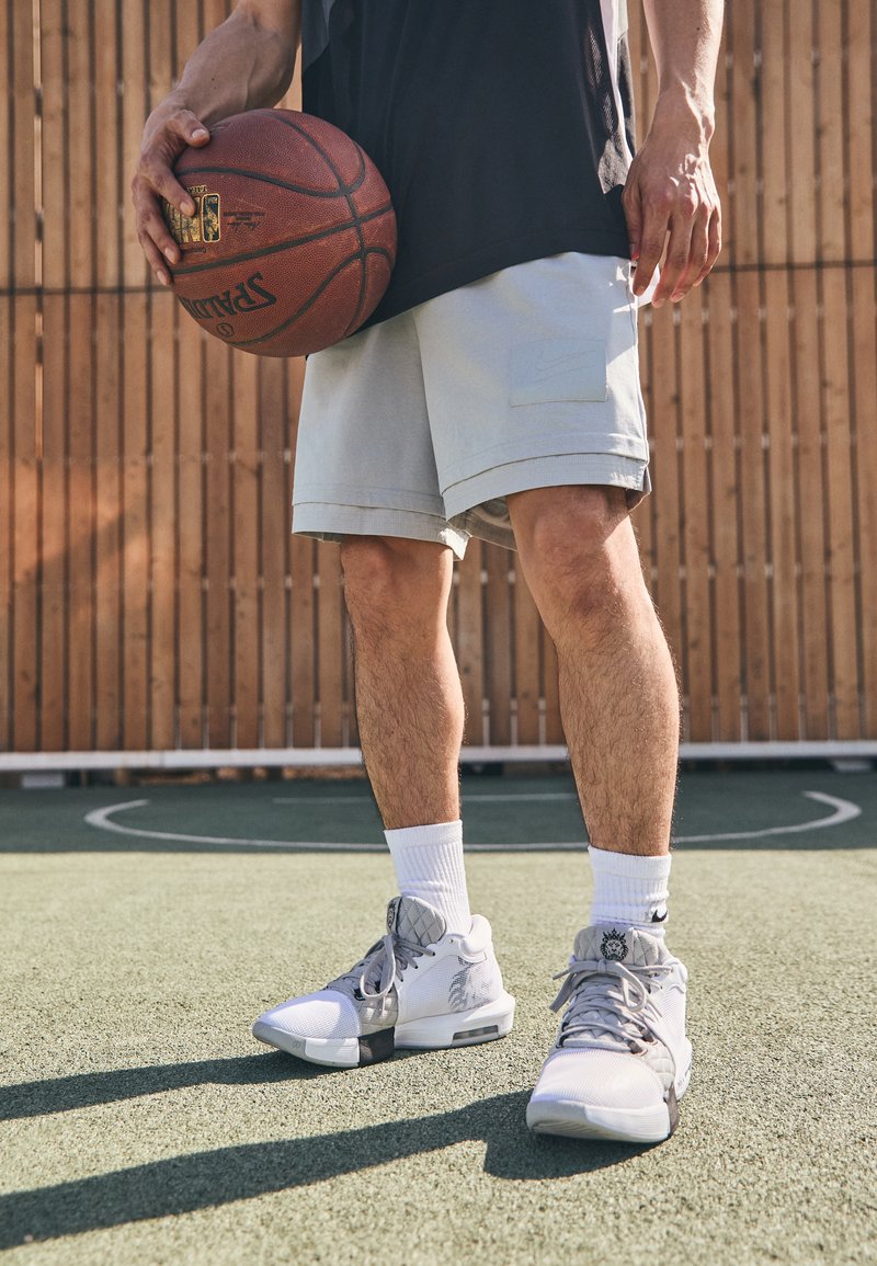 Light gray athletic shorts with side pocket, paired with white and gray sneakers featuring mesh and rubber details, holding a basketball.
