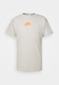 Beige short-sleeve Nike T-shirt with orange logo centered on the chest, displayed on a plain white background.