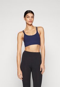 Navy blue crop top with thin, double straps; made of smooth, stretchy fabric; features a rounded neckline and a cropped fit.
