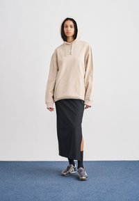 Μπεζ φαρδιά φούτερ, μαύρη μάξι φούστα με πλαϊνή σχισμή, μαύρες κάλτσες και γκρι αθλητικά παπούτσια με λευκές ρίγες. Απλός και μοντέρνος σχεδιασμός.