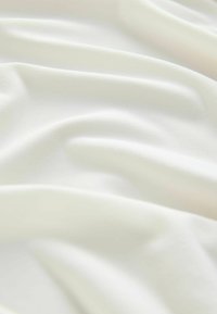 Soft, matte white fabric with a smooth texture, featuring gentle folds and creases, indicating drape and fluidity.