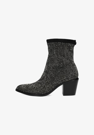 Bottines noires avec un haut côtelé ajusté, recouvertes de clous en métal, et un talon épais. Caractérisées par un bout pointu et une silhouette élégante.