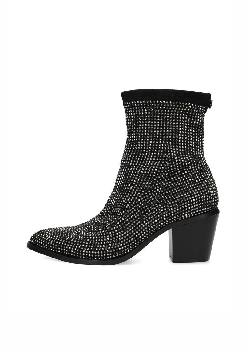 Černá kotníková bota s přiléhavým žebrovaným svrškem, pokrytá kovovými cvoky, a masivním podpatkem. Disponuje špičatou špičkou a elegantním siluetou.