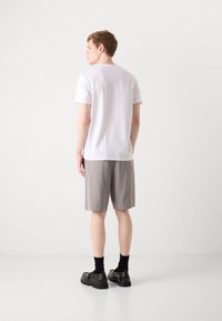Baltas trumpa rankovė t-shirt, pilkos kelnės iki kelių, juodi batai su kojinėmis. Minimalistinis dizainas, lygus paviršius ir neutralios spalvos.