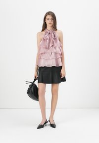 Ljusrosa ärmlös topp med lager av volanger och knytning vid halsen. Svart kjol, svart handväska och spetsiga klackskor fulländar outfiten.