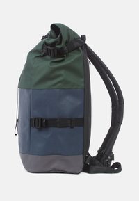 Grön och marinblå rulltopp ryggsäck med en grå botten. Har justerbara remmar, en sidspänne och en texturerad vattentät yta.