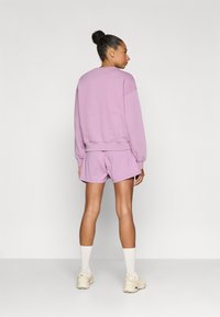 Μωβ φούτερ με ραμμένους ώμους, σετ με ταιριαστά μωβ σορτς. Το μοντέλο φοράει λευκές κάλτσες και μπεζ αθλητικά παπούτσια. Ομαλή υφή.