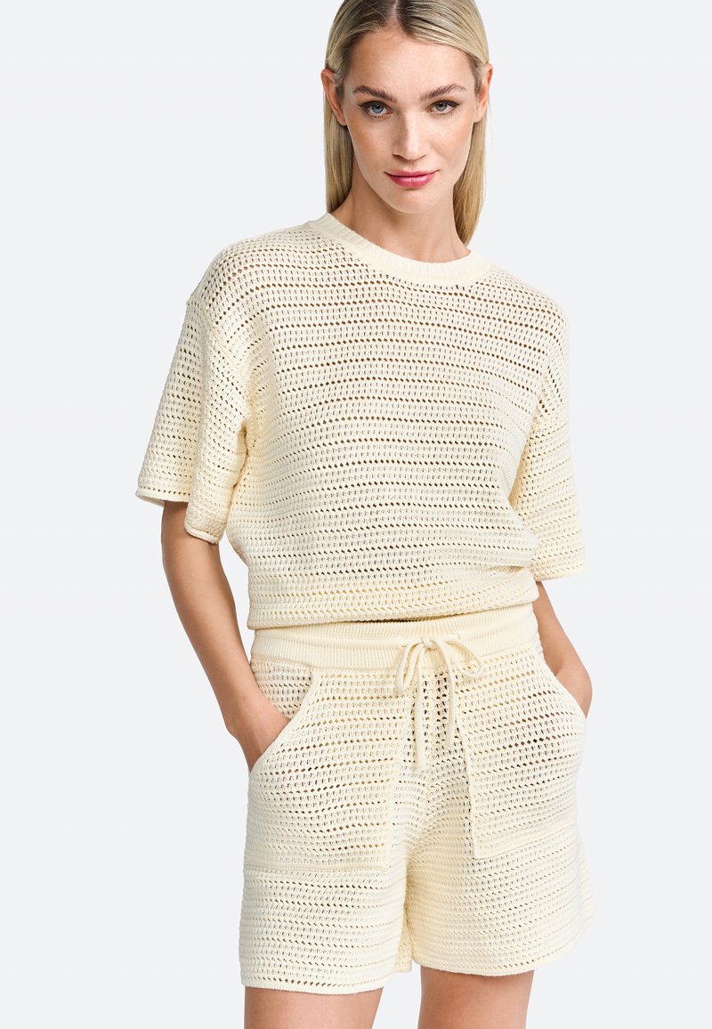 Knit short set in light cream. Top: loose fit, round neckline, short sleeves. Shorts: elastic waist with drawstring, side pockets, textured design.