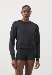 Zwarte Nike sweatshirt met lange mouwen en cropped design, met een klein logo op de borst. Gecombineerd met zwarte shorts met stippenaccenten.
