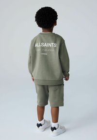 Vihreä puuvillainen huppari, jossa valkoinen "ALLSAINTS"-teksti, ja shortsit. Hupparissa on resorit hihansuissa ja helmassa. Yhdistetty valkoisiin lenkkareihin.