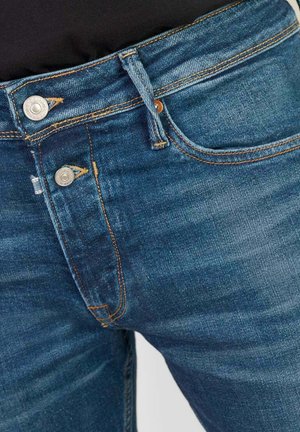 Blauwe denim jeans met een middelhoge taille, zichtbare stikdetails, twee metalen knopen en een gestructureerde afwerking.