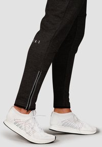 Gray athletic joggers with zippers and white lettering, paired with white, breathable knit running shoes featuring a textured upper.