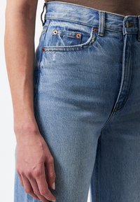 Vaaleansinisiä farkkuja, joissa on korkea vyötärö, kuparinvaihtavat, haalistunut pinta ja vasemmalla puolella näkyvä etutasku.