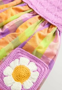 Robe colorée avec un corsage en crochet rose à motif texturé et une jupe à carreaux multicolore dans des teintes d'orange, de vert et de violet, accentuée par un motif de marguerite.