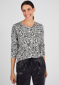Cardigan a stampa zebra bianco e nero realizzato in tessuto morbido, con scollatura rotonda e chiusura a bottoni, abbinato a pantaloni in ecopelle neri.