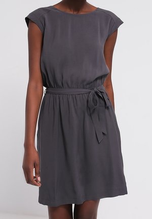Mujer con vestido sin mangas gris oscuro hasta la rodilla, con escote redondo y cinturón de tela anudado en la cintura.