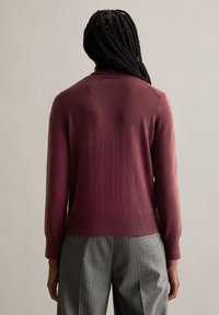 Burgundy színű pulóver, fitted bordás aljjal és hosszú ujjakkal, puha anyagból készült. Magas nyakkivágással és sima felülettel rendelkezik.