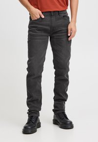 Tumedat halli teksastiiliga teksad, millel on kitsas lõige, viie taskuga disain ja peen toon-toonis õmblus, mida on kombineeritud mustade pits-up saabastega.