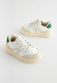 Baskets blanches avec des accents beiges et un talon en verde. Elles présentent une tige en cuir texturé, une languette rembourrée et une semelle en caoutchouc avec une bonne adhérence.