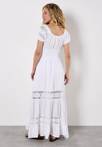 Witte maxi-jurk met korte pofmouwen, smock-borstvoeding en kanten randen. Vloeiende stof met een tiered rok ontwerp.