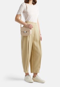 Proužkovaná košile s krátkým rukávem, béžové široké kalhoty a bílé tenisky. Béžová kabelka přes rameno s kovovou sponou, hladkým povrchem a minimalistickým designem.