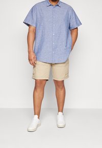 Světle modrá košile s krátkým rukávem a knoflíky, khaki cargo šortky a bílé tenisky. Košile má volný střih a strukturovanou tkaninu.