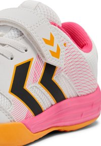 Witte sportschoen met een ademende mesh bovenkant, zwarte en oranje accenten, en een roze zool met een klittenbandsluiting voor een veilige pasvorm.