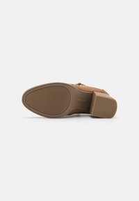 Brown heeled shoe with a textured sole, smooth upper material, and a side zipper. Features a block heel for stability.