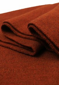 Tessuto color ruggine piegato con cura, che mostra una consistenza morbida e un fine motivo a maglia. Il materiale appare caldo e spesso, adatto per l'abbigliamento.