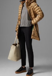 Doudoune dorée avec une capuche, pull en maille noir et blanc à motifs, pantalon noir ajusté, baskets noires et un sac fourre-tout crème.