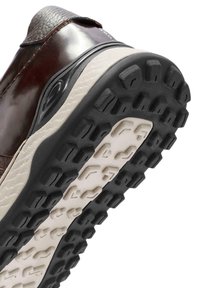 Sneaker in pelle marrone con tomaia testurizzata, intersuola crema e suola in gomma nera con un motivo di lugs esagonali per una migliore aderenza.