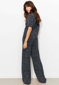 Combinaison noire à coupe ample avec manches courtes, motif subtil et jambes larges. Tissu lisse avec une texture douce.