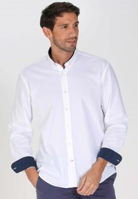 Chemise blanche à manches longues avec des poignets contrastants bleu marine et un col classique. Tissu lisse avec une coupe ajustée.