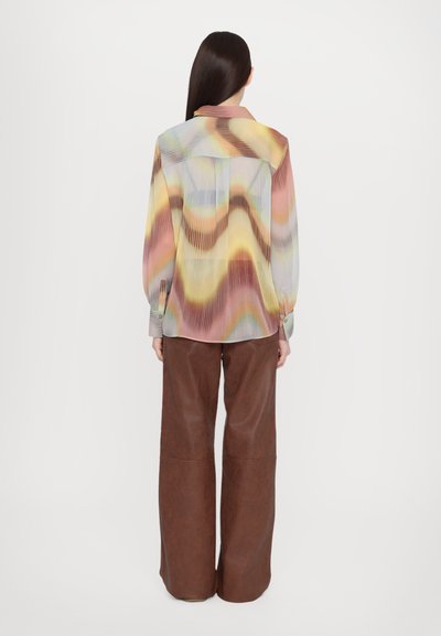 Bluză plisată multicoloră cu un model de valuri în nuanțe de roz, galben și albastru; mâneci lungi și guler. Pantaloni brown evazați.