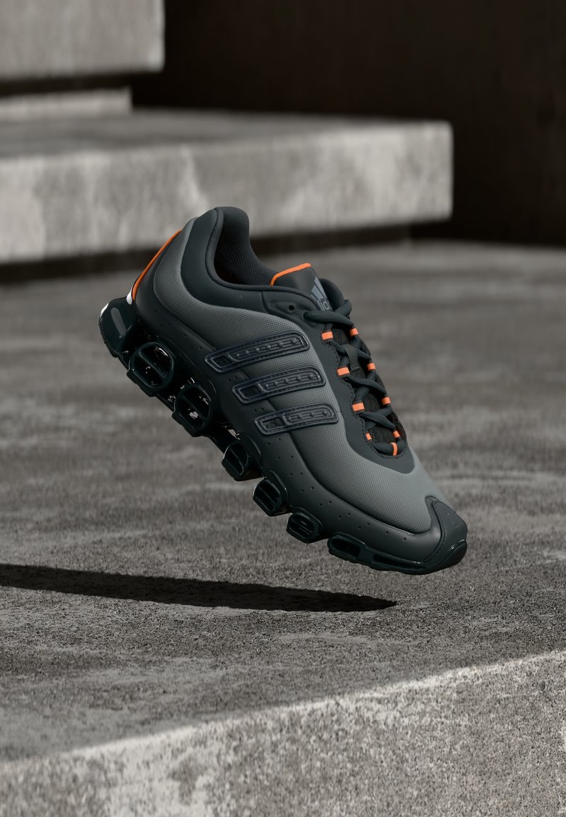 Tumesinine sportkingad tekstureeritud pealispinnaga, oranžide detailidega ja nähtavate õhumullidega tallal. Silmapaistev kolme triibuga disain.