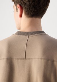 Beige sweatshirt featuring a ribbed crew neck, subtle seam detailing on the back, and a smooth texture.