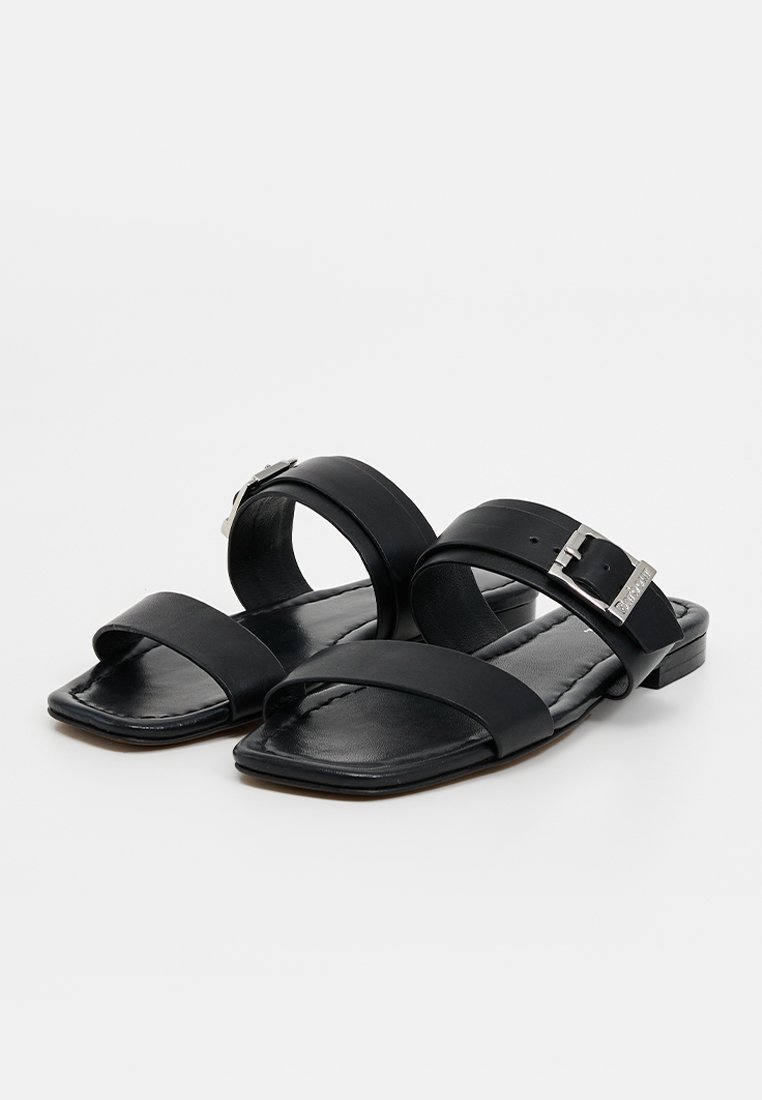 Czarne skórzane sandały z dwiema szerokimi paskami i metalowym zapięciem. Płaska podeszwa o kwadratowym kształcie czubka i gładkiej fakturze.