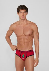 Czerwone męskie slipy z czarnym pasem, z grafiką choinki i napisem "Rockin' Christmas". Wykonane z elastycznego materiału.