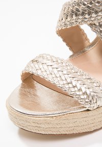 Espadrille doré métallique avec des sangles tressées et une semelle en jute tissée. Dispose d'un dessus lisse et d'une plateforme plate.