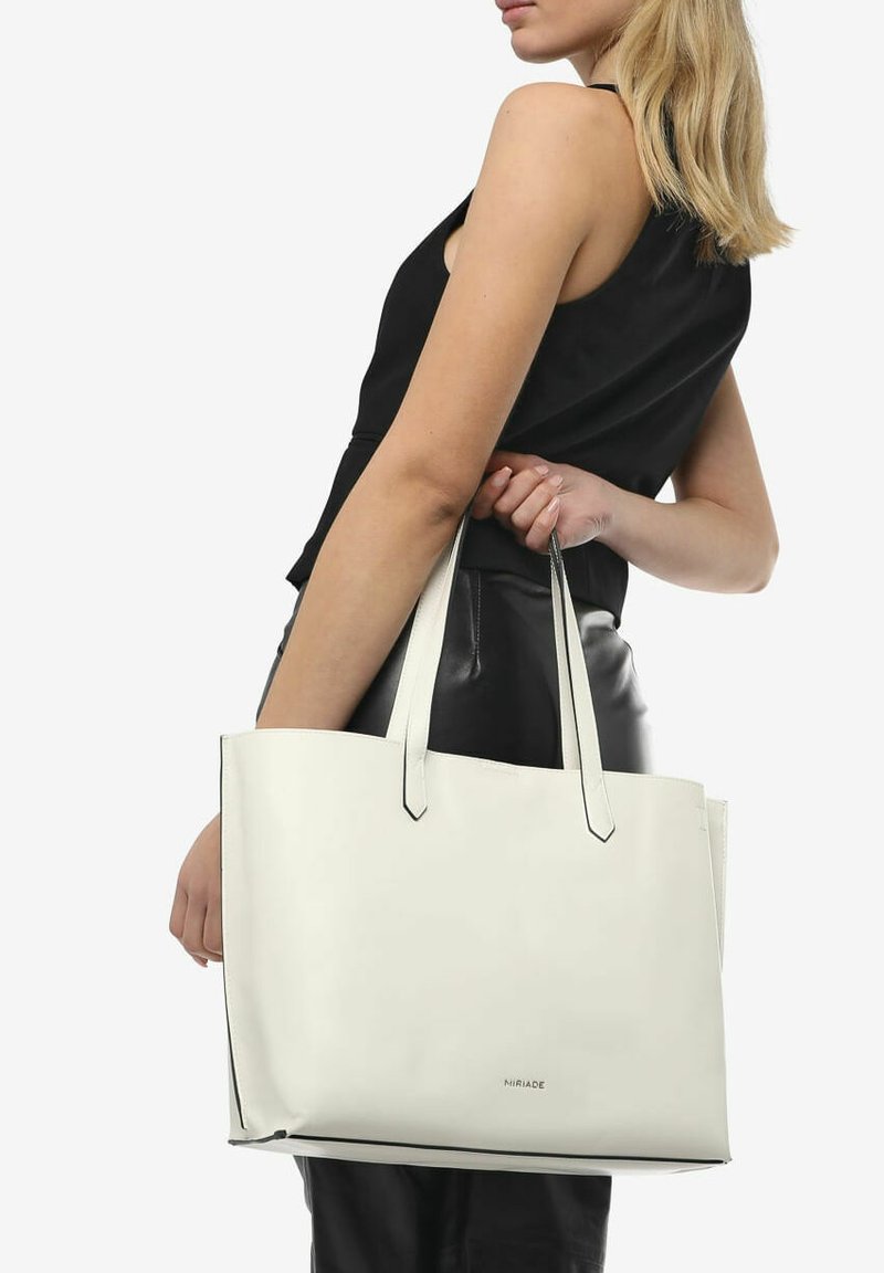 Witte leren tote bag met een minimalistisch ontwerp, contrasterende zwarte accenten en een platte, verlengde vorm. Voorzien van twee stevige handvatten voor vervoer.