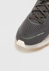 Scarpa da running Nike in rete grigia scura con accenti neri, dotata di un colletto imbottito, superficie текстurizzata e suola bianca con un leggero rialzo del tacco.