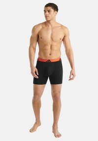 Černé pánské trenýrky s oranžovým pasem, na kterém je logo. Tkanina vypadá hladce a pružně, navržena pro pohodlí a dokonalé padnutí.