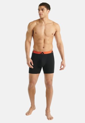 Schwarze Herrenboxershorts mit einem orangen Bund, der ein Logo trägt. Der Stoff wirkt glatt und dehnbar, konzipiert für Komfort und eine gute Passform.