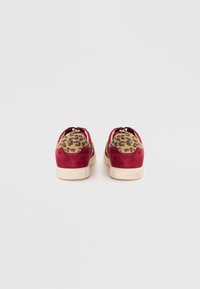 Red suede sneakers with a leopard print fabric back panel, featuring a cream rubber sole and matching laces. Textured accents enhance design.