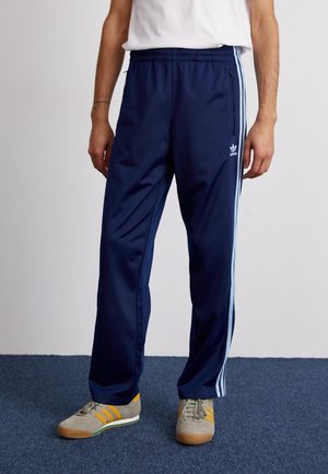 Donkerblauwe sportbroek met elastische tailleband, zijzakken en lichtblauwe strepen langs de zijkanten. Gemaakt van gladde, lichte stof.